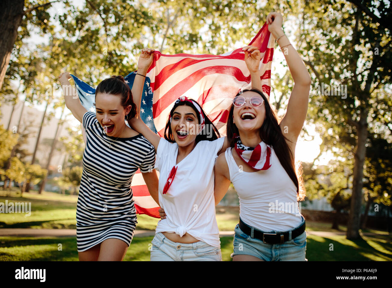Allegro amici di sesso femminile che corre attorno al parco con bandiera americana. Giovane ed entusiasta ragazze americano godendo il 4 luglio vacanza al parco. Foto Stock