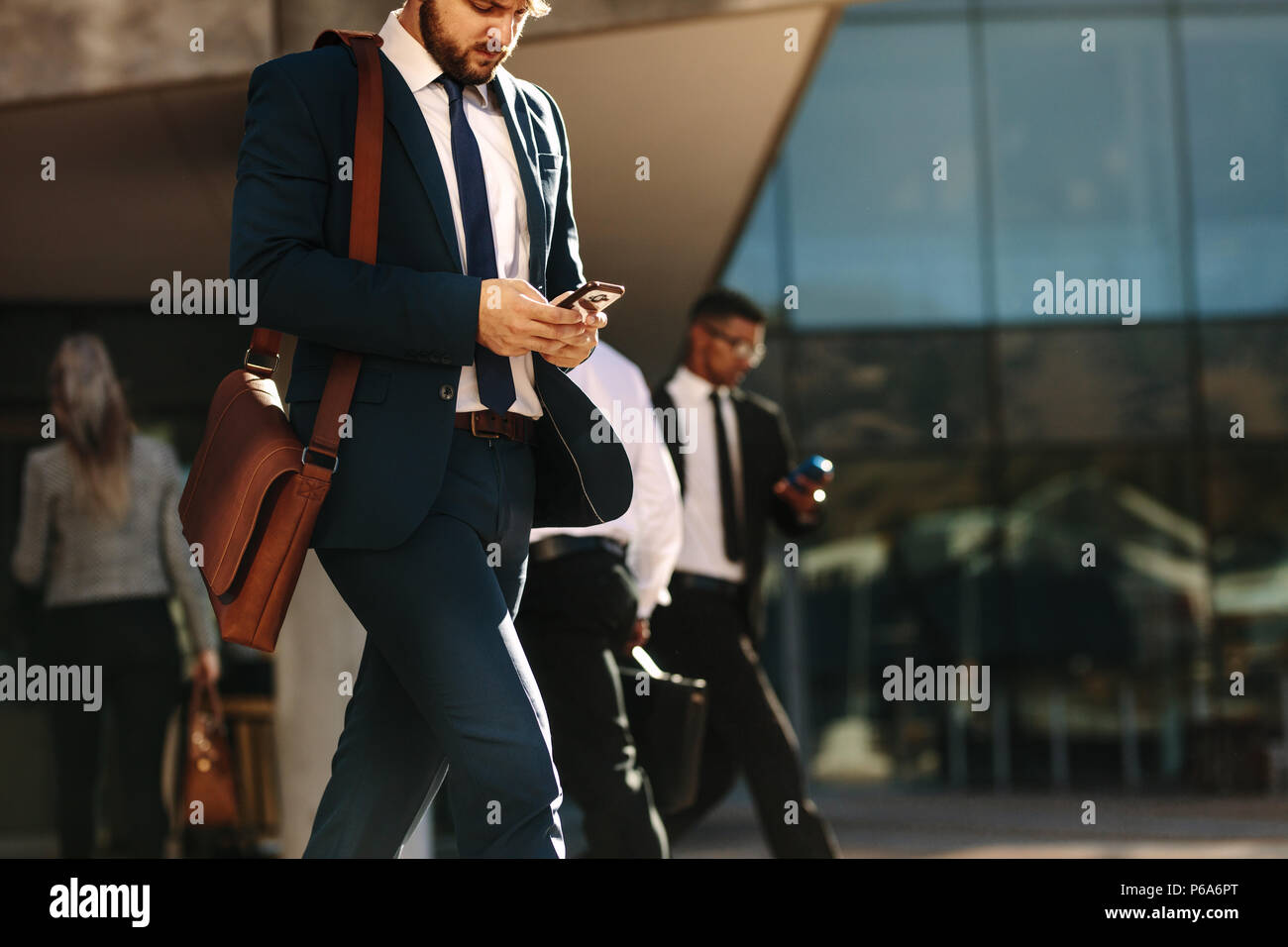 Imprenditore in abiti formali che trasportano borsa da ufficio tramite telefono cellulare durante gli spostamenti per l'ufficio. Ufficio occupato andando le persone che usano i loro telefoni cellulari whi Foto Stock