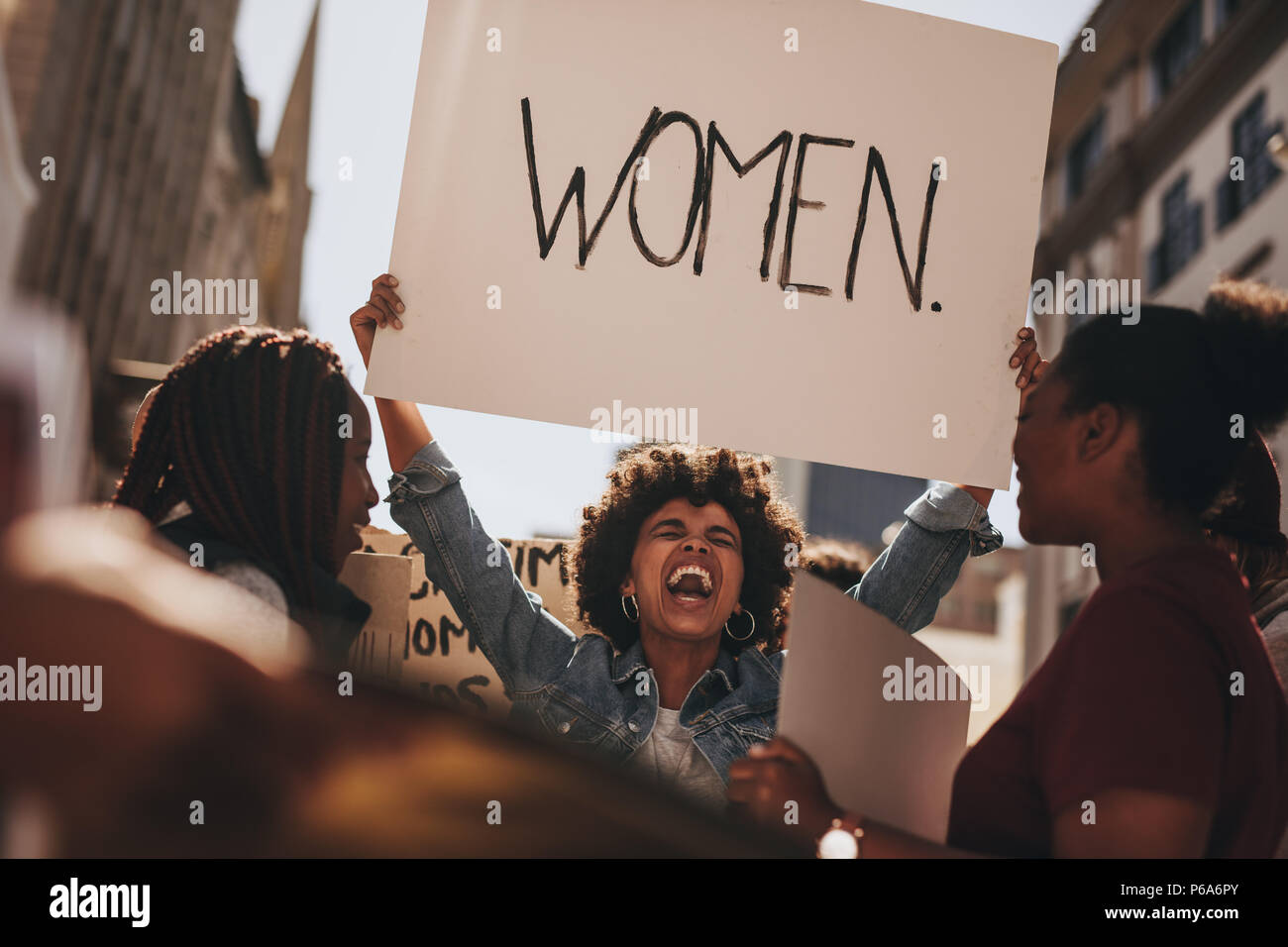 Donna africana tenendo un banner e ridere durante le donne di marzo. Gruppo femminile di dimostrare all'aperto con cartelli. Foto Stock