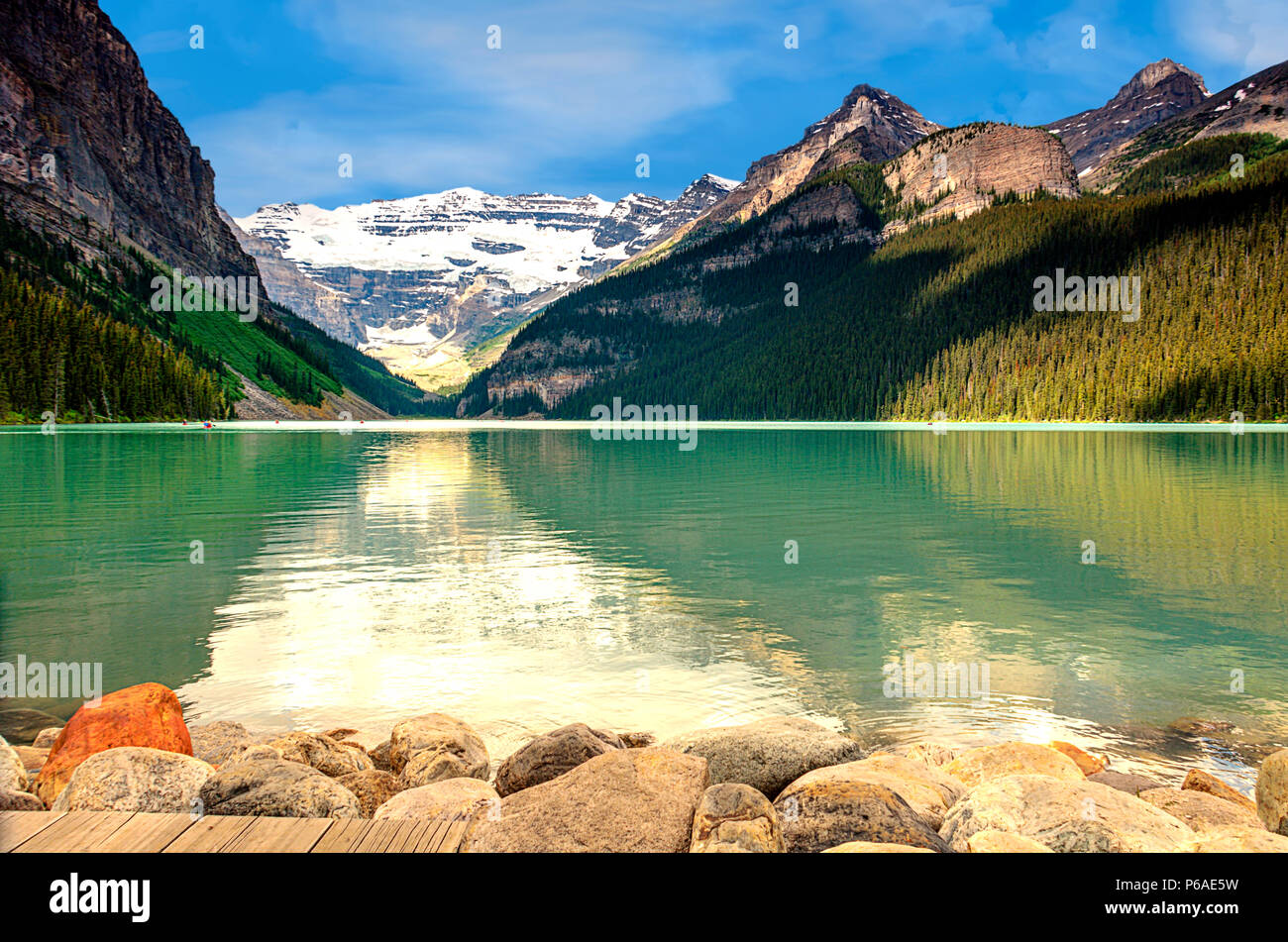 Una vista del lago verde smeraldo e montagne innevate. Foresta sulle piste, di pietre e di pavimenti in legno, cielo blu con nuvole bianche, su un estate da Foto Stock