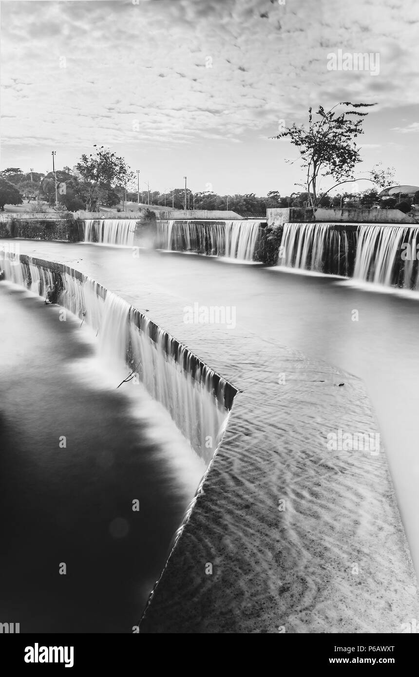 Cascate artificiali di acqua di lago e di un parco con la natura intorno. Una lunga esposizione, foto in bianco e nero di un parco a Campo Grande MS, Brasil. Foto Stock
