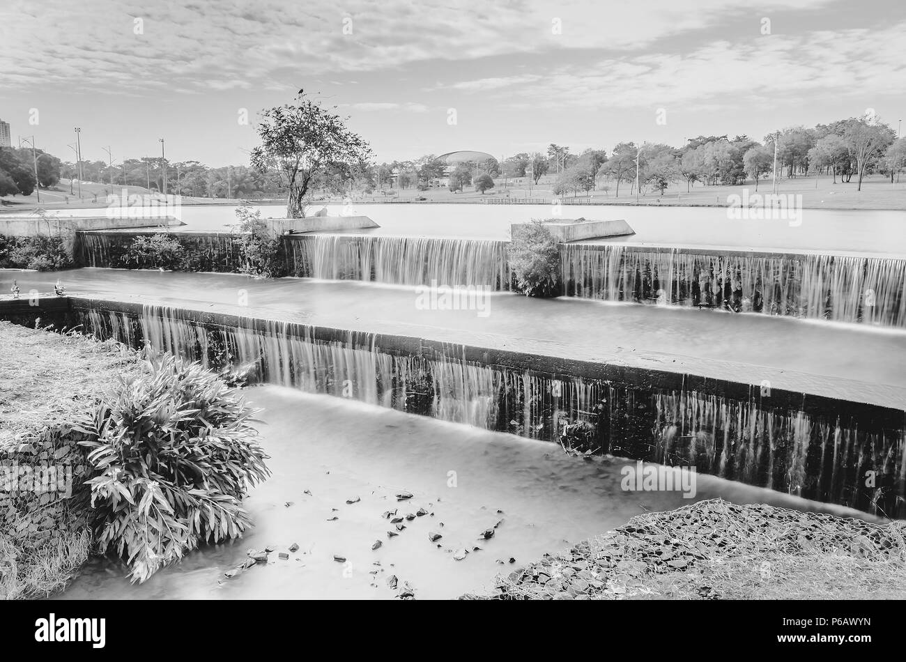 Cascate artificiali di acqua di lago e di un parco con la natura intorno. Una lunga esposizione, foto in bianco e nero di un parco a Campo Grande MS, Brasil. Foto Stock