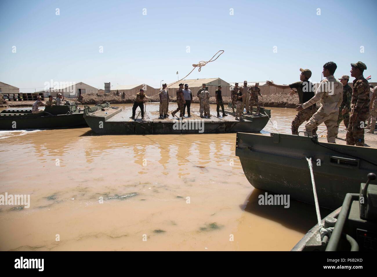 Un soldato iracheno assegnato all'esercito iracheno reggimento di bridging getta una legatura della fune a un compagno soldato durante il ponte di flottazione della formazione di Camp Taji, Iraq, 21 aprile 2016. Il 502nd multiruolo Bridge mission dell'azienda è quello di distribuire in tutto il mondo per eseguire a livello strategico il supporto logistico ad un teatro di operazioni di apertura e di mantenimento di critici di linee di comunicazione attraverso infrastrutture di bridging e conducendo fisso e ponte galleggiante operazioni. Abilitando le forze di sicurezza irachene attraverso la consulenza e assistenza e la costruzione di capacità del partner missioni, la Combined Joint Task Force - Funzionamento Inhe Foto Stock
