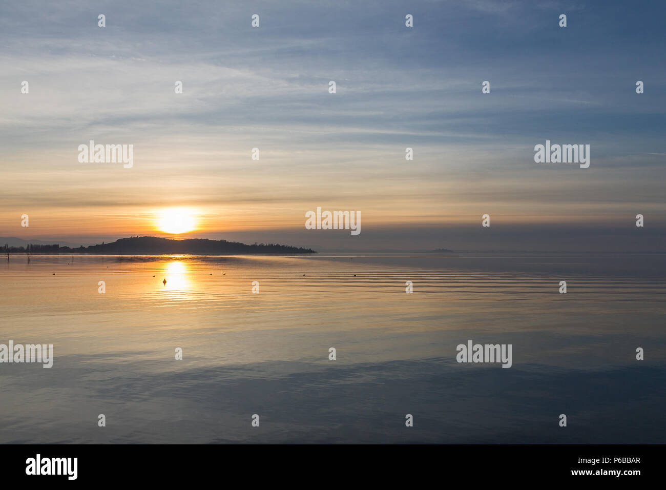 Una ripresa di un tramonto su un lago, con il sole che scende dietro un'isola Foto Stock