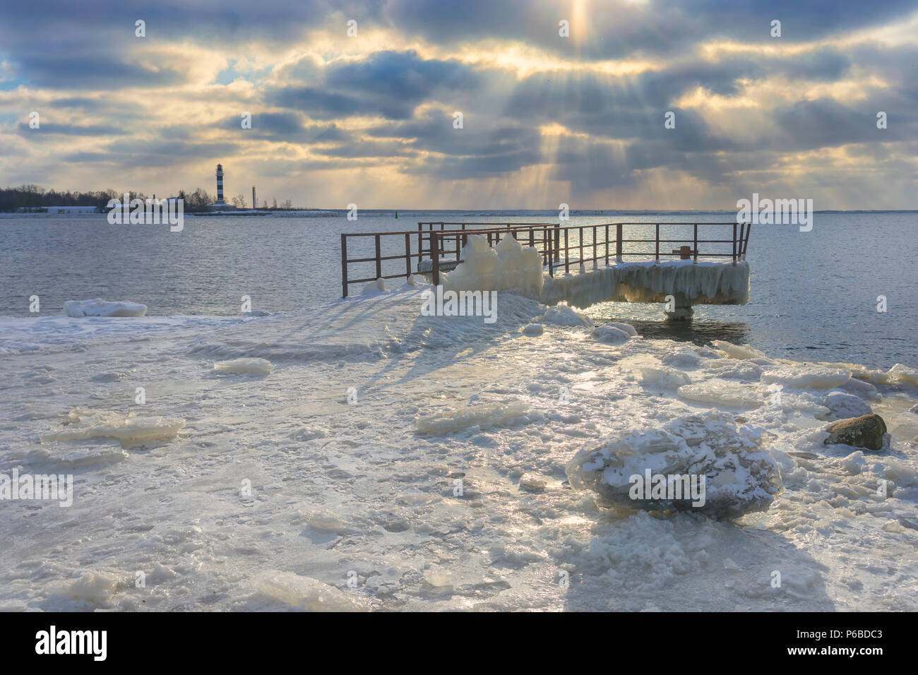 Ormeggio nel ghiaccio contro il faro alla foce del fiume nei pressi del Mar Baltico con raggi del sole attraverso le nuvole in inverno Foto Stock