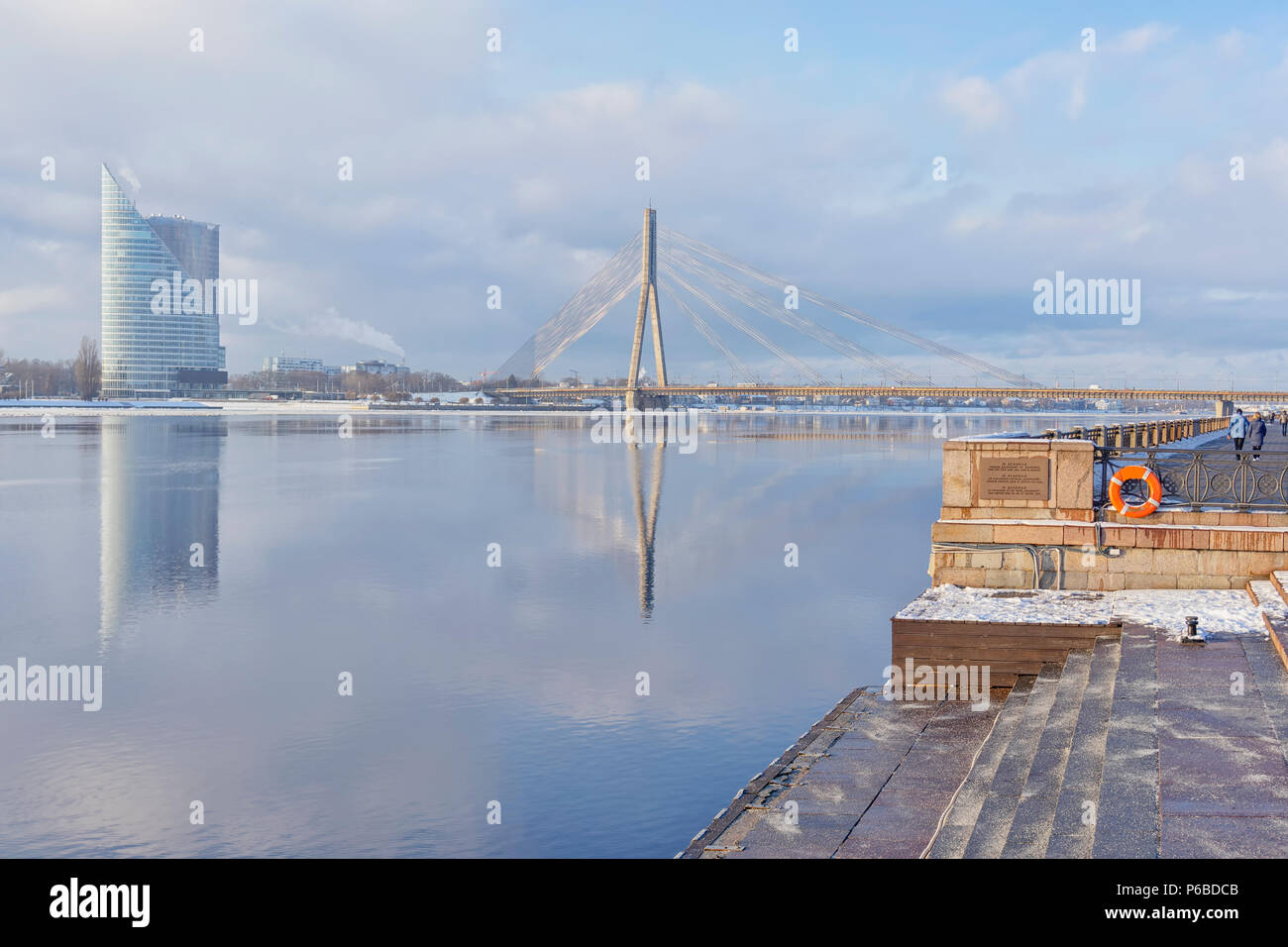 La Riga terrapieno vicino al fiume Daugava in un inverno gelido Giornata contro lo sfondo di un grattacielo e un cavo-alloggiato in parallelo con la riflessione Foto Stock
