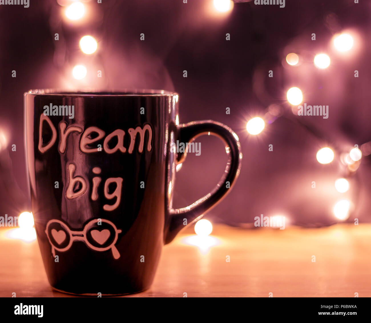 Tazza da caffè con lettere grandi sogni con vapore su di un piano in legno e Natale piccole luci su uno sfondo scuro. Copyspace. Vista frontale Foto Stock