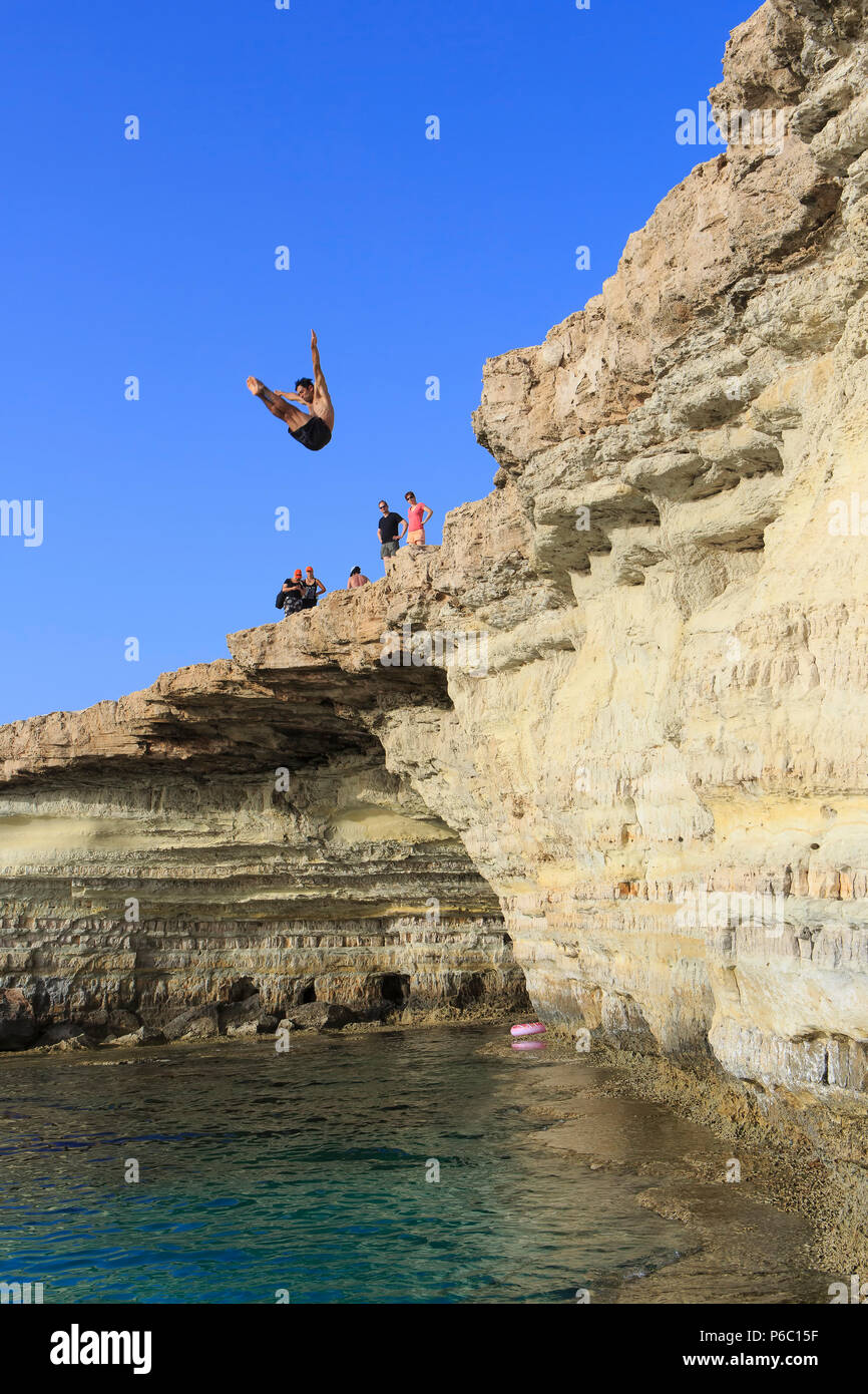 Un maschio sub diving dalle scogliere in all'acqua turchese al mare grotte nei pressi di Cape Greco, Cipro Foto Stock