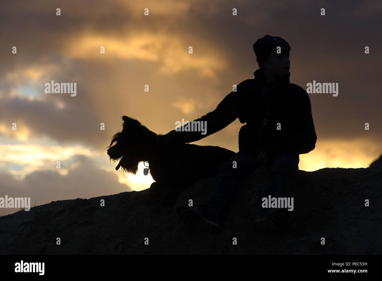 Wustrow, Germania - Silhouette, ragazzo seduto in serata con il suo cane su una duna Foto Stock