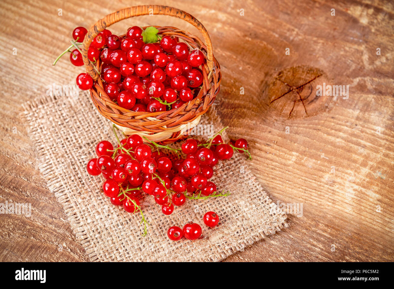 Ribes rosso nel cesto marrone sul tavolo di legno. Frutti freschi ribes rosso sul tavolo. Foto Stock