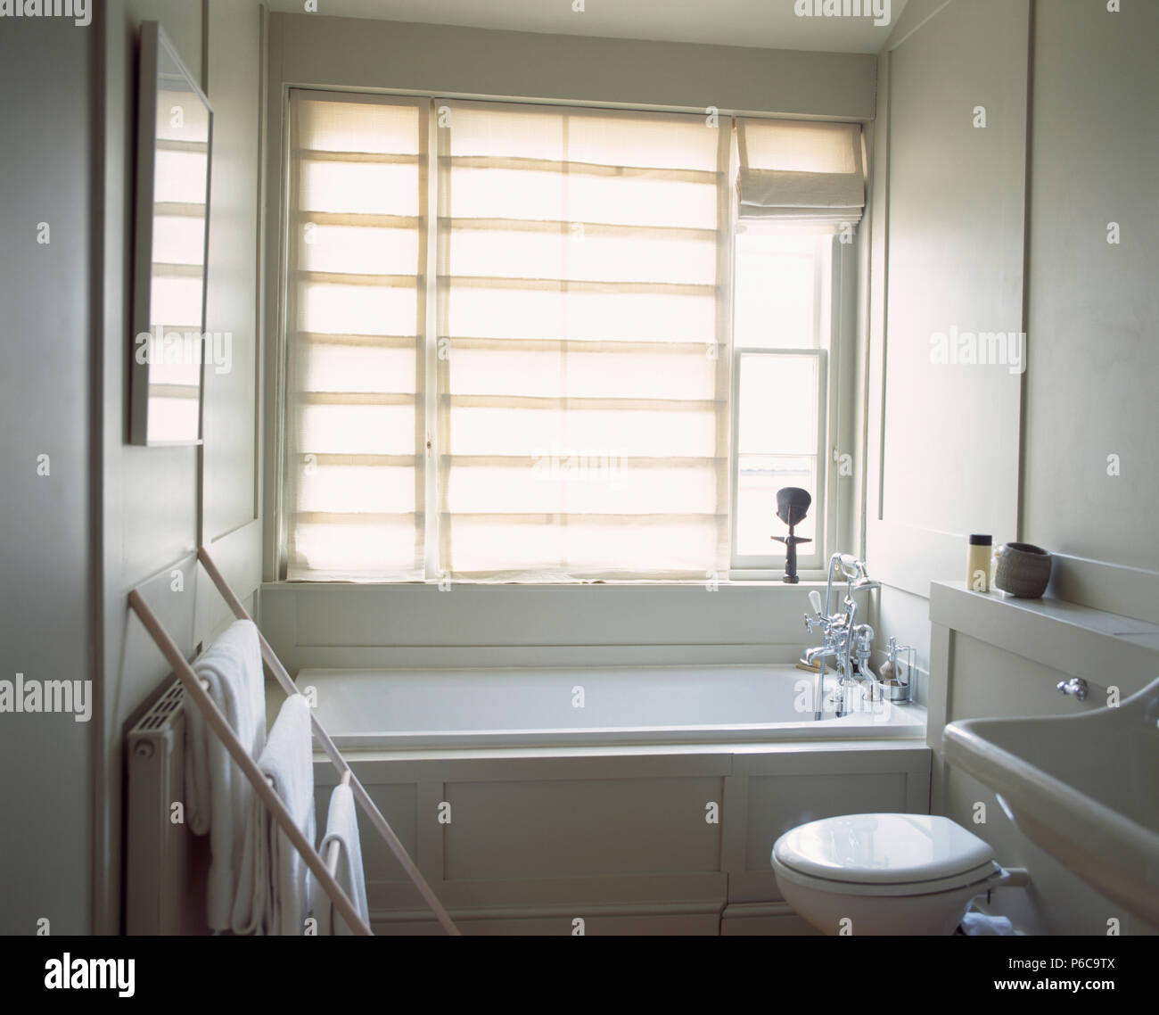 Biancheria da letto bianca Roman cieco sulla finestra sopra bagno in piccole stanze da bagno di colore bianco con asciugamani bianchi su semplici rack in legno Foto Stock