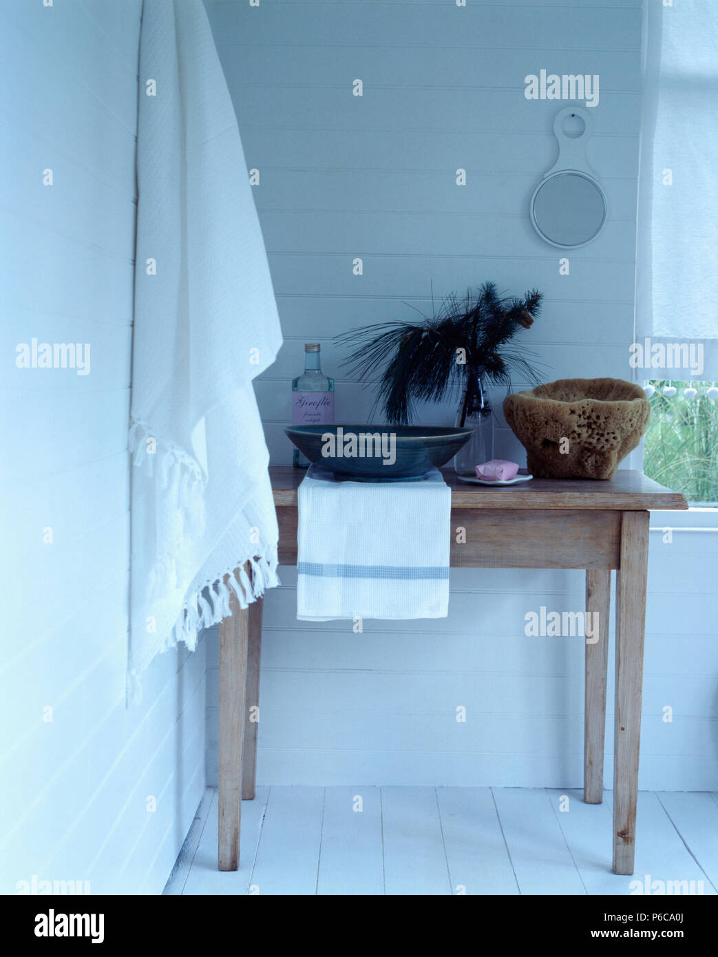 Asciugamano bianco appesa alla parete accanto al piccolo tavolo in legno con recipiente di ceramica in un semplice bagno bianco Foto Stock