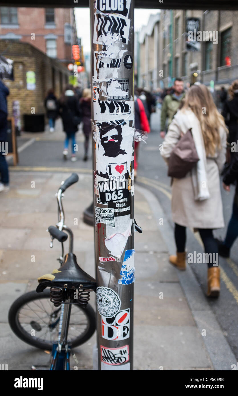 Street View di segno posto nel quartiere alla moda di Brick Lane decorata con una varietà di adesivi artistico e con una BMX appoggiata contro di esso. Londra, Inghilterra. Foto Stock