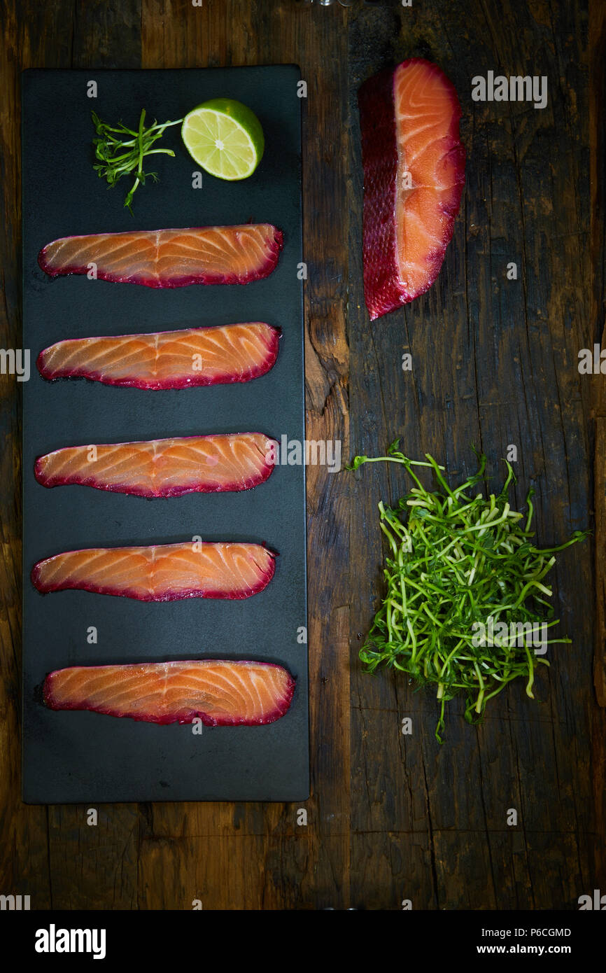 Fette di filetto di salmone, salate con succo di barbabietola, servita su tutto il frumento con foglie di insalata, sale marino e pepe su una superficie metallica. Vista dall'alto. Foto Stock