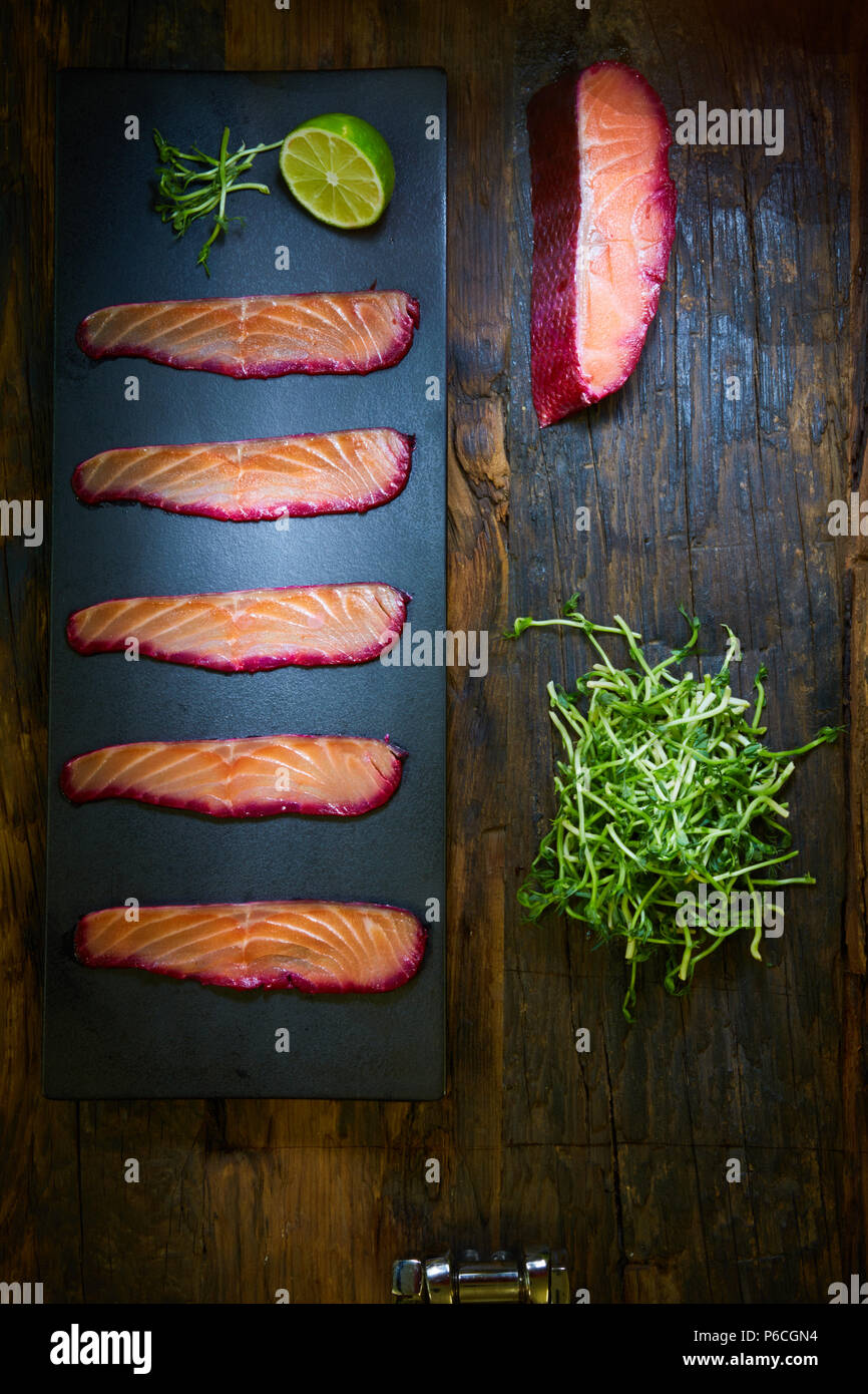 Fette di filetto di salmone, salate con succo di barbabietola, servita su tutto il frumento con foglie di insalata, sale marino e pepe su una superficie metallica. Vista dall'alto. Foto Stock
