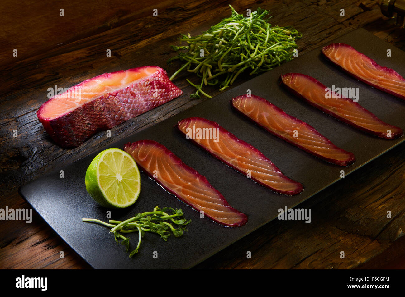 Fette di filetto di salmone, salate con succo di barbabietola, servita su tutto il frumento con foglie di insalata, sale marino e pepe su una superficie metallica. Vista dall'alto. Foto Stock