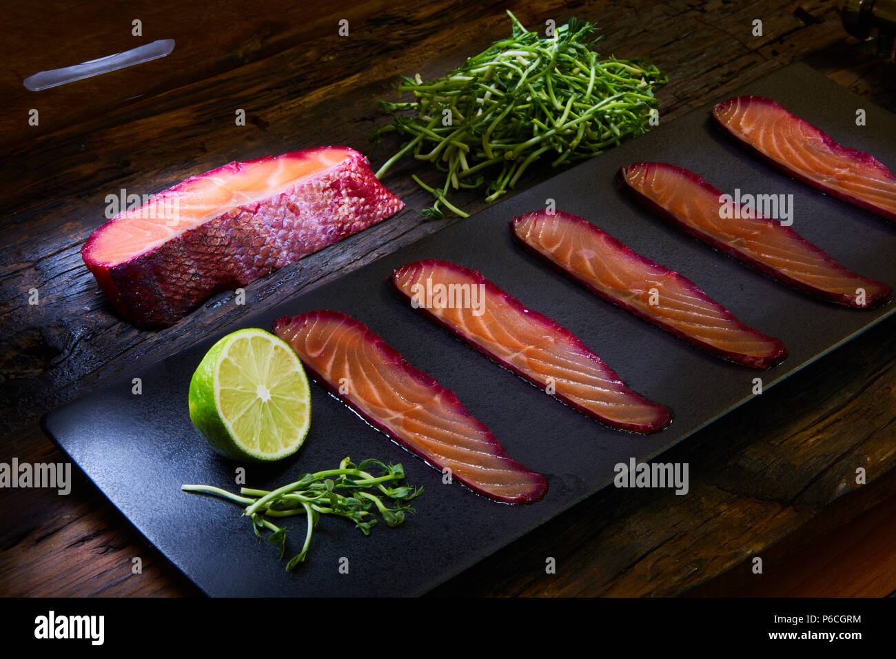 Fette di filetto di salmone, salate con succo di barbabietola, servita su tutto il frumento con foglie di insalata, sale marino e pepe su una superficie metallica. Vista dall'alto. Foto Stock