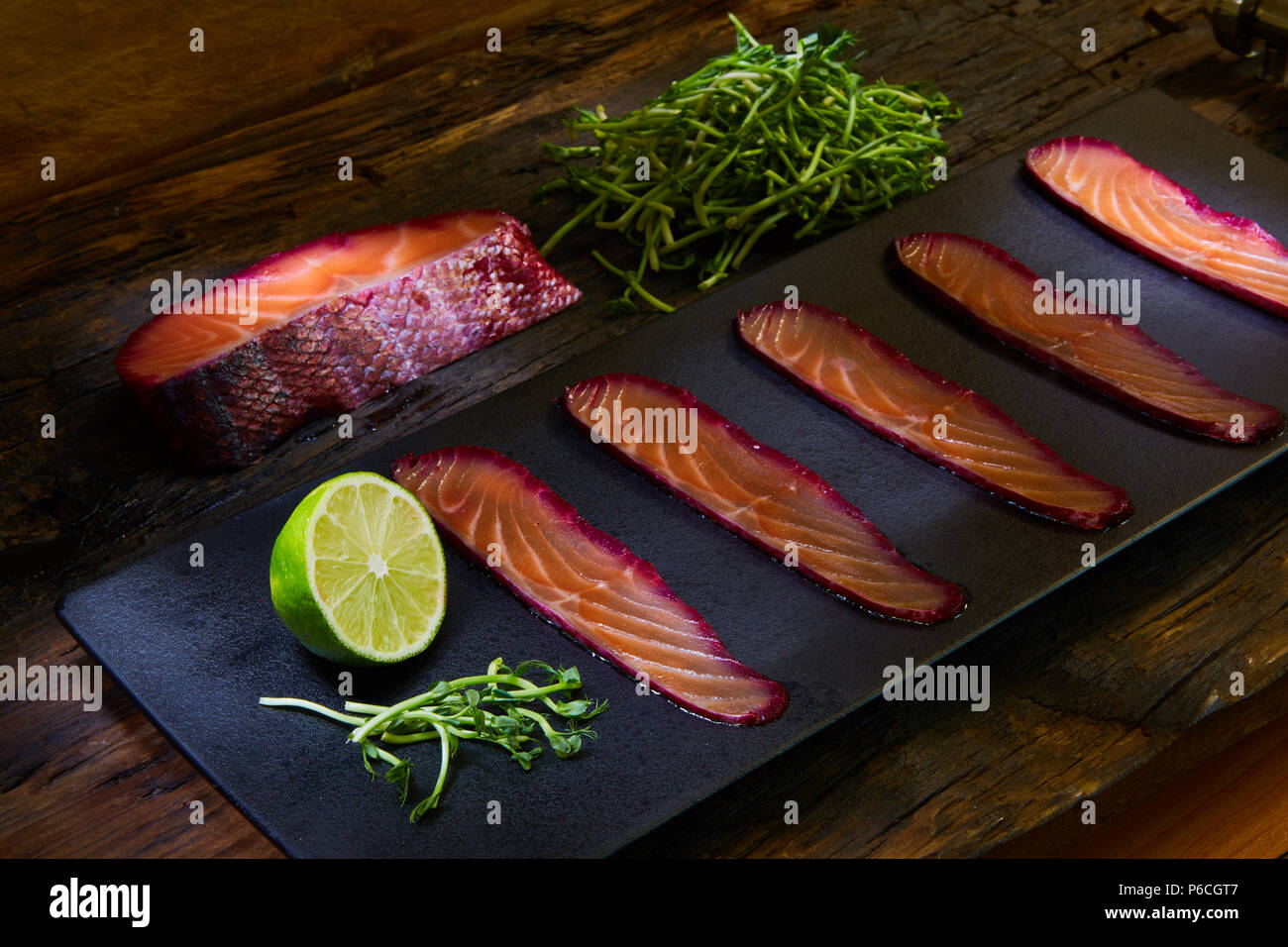 Fette di filetto di salmone, salate con succo di barbabietola, servita su tutto il frumento con foglie di insalata, sale marino e pepe su una superficie metallica. Vista dall'alto. Foto Stock