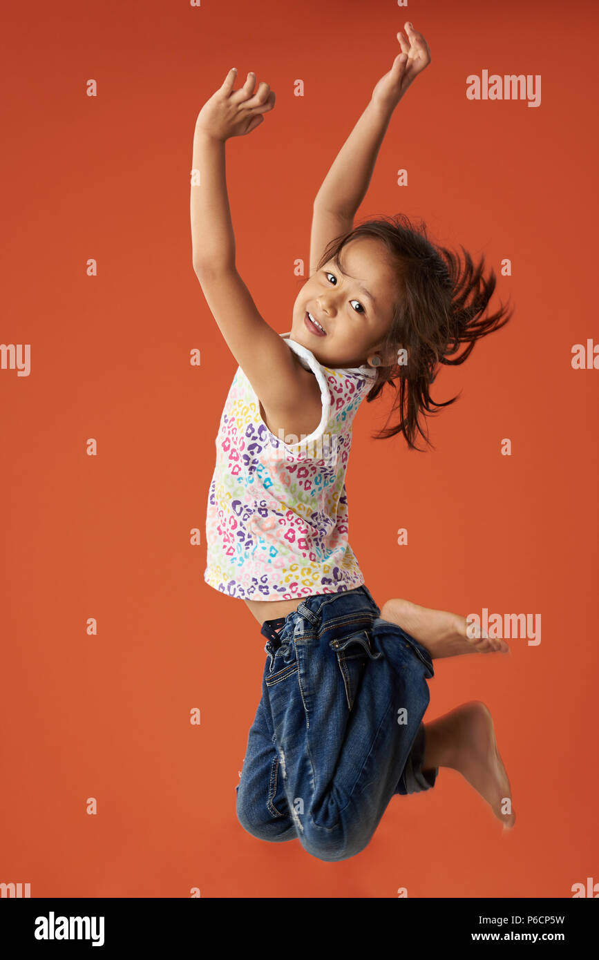 Piccola ragazza asiatica saltare in aria isolata su sfondo arancione Foto Stock