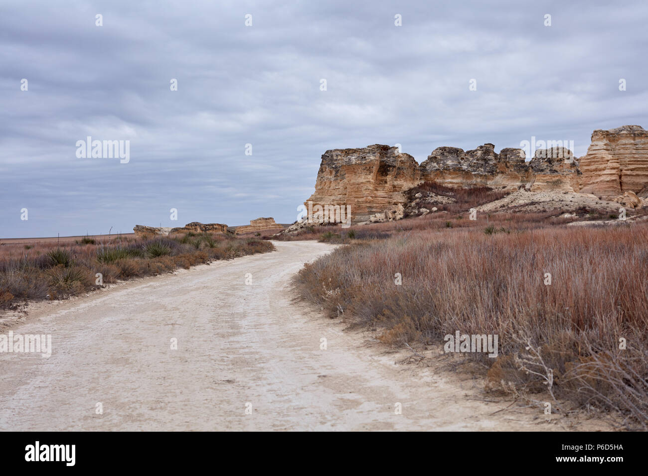 Avvolgimento su strada sterrata in Castle Rock badlands, Kansas che conduce alla pietra calcarea erosa formazioni rocciose attraverso pascoli della prateria Foto Stock