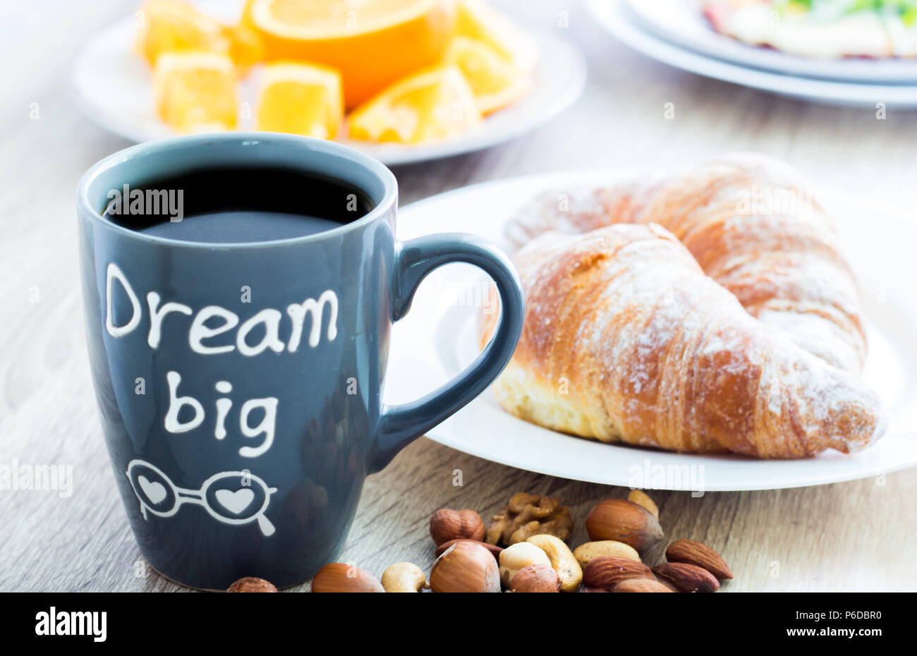 Grande Sogno. Una buona prima colazione al mattino. La tazza di caffè con croissant, dadi e fresche arance a fette Foto Stock