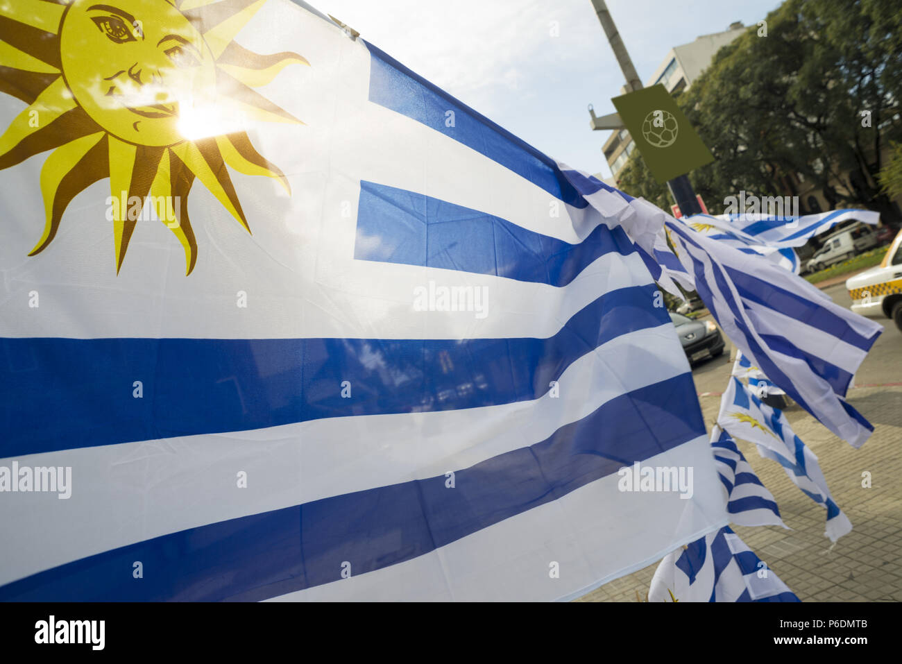 Bandiera uruguayano in strada di città con pallone da calcio poster sullo sfondo. Uruguay paese emblema nazionale. Foto Stock