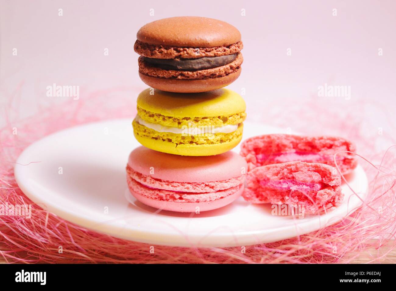Marrone, giallo e rosa amaretti pila di colori pastello in piedi su una piccola piastra bianca e rosa sfondo decorativo. Vista frontale. Foto Stock