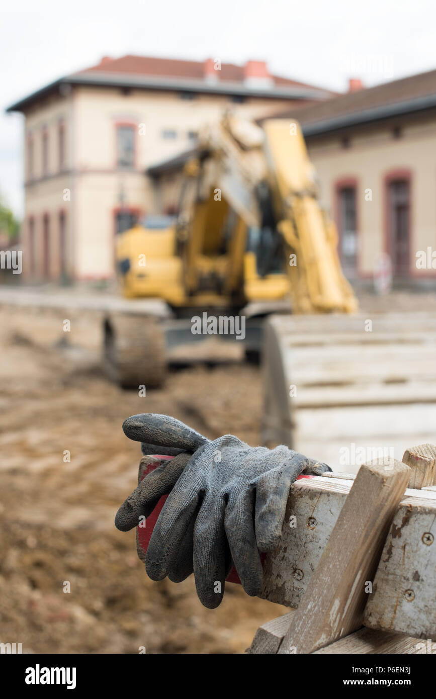Vecchio e sporco e guanti neri in cantiere con grande escavatore giallo in background. Foto Stock