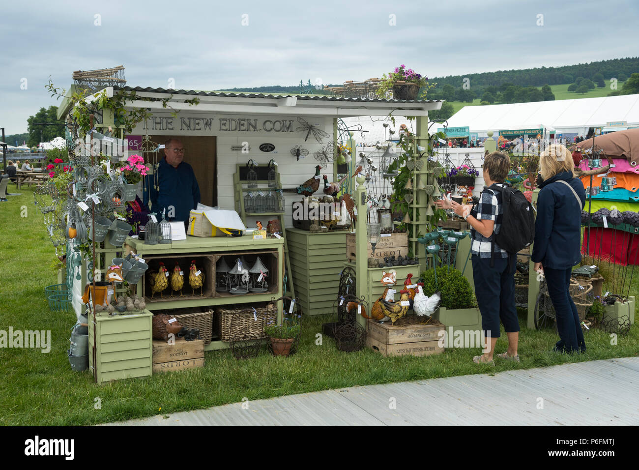 2 donne in piedi, guardando il display del giardino scultura & ornamenti in stallo a RHS Chatsworth Flower Show, la Chatsworth House, Derbyshire, England, Regno Unito Foto Stock