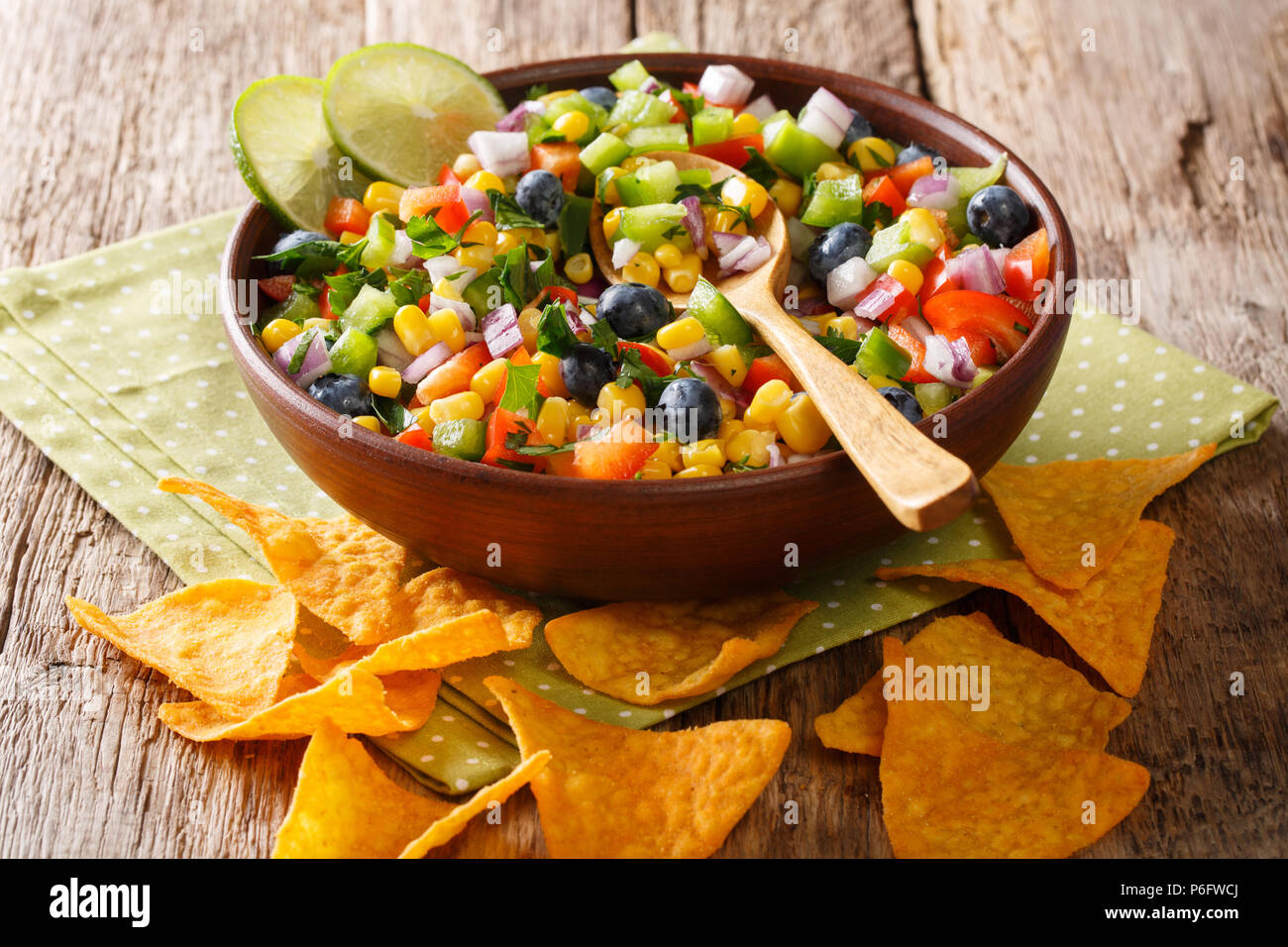 Snack insalata di mais, mirtilli, peperoni, erbe e cipolle close-up in una ciotola e nachos chips sul tavolo orizzontale. Foto Stock