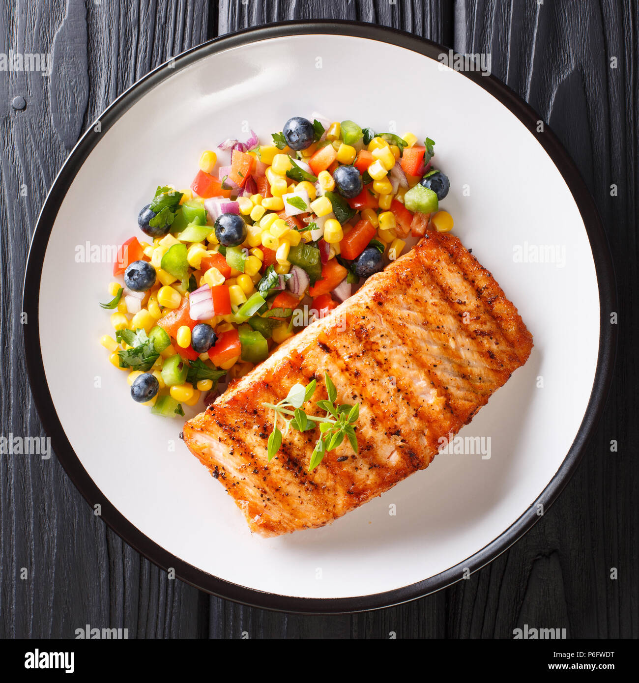 Filetto di salmone alla griglia con insalata di salsa di verdure e mirtilli close-up su una piastra su un tavolo. vista in pianta da sopra Foto Stock Filetto di salmone alla griglia con insalata di salsa di verdure e mirtilli close-up su una piastra su un tavolo. vista in pianta da sopra Foto Stock