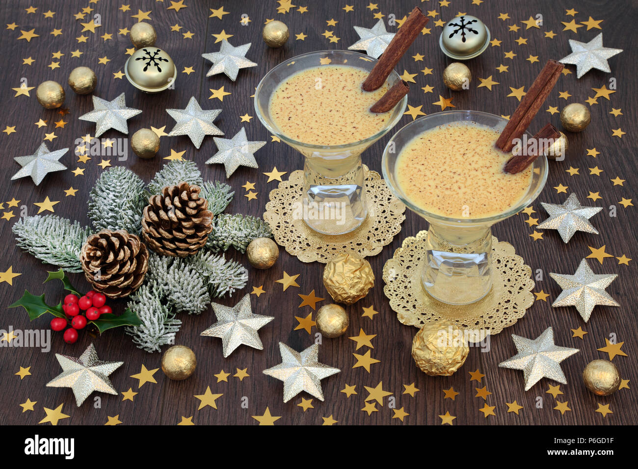 Zabaione di Natale bevande in bicchieri con stella in oro e decorazioni a campana, stagnola avvolto le sfere di cioccolato con l'inverno flora di holly, abete e pino coni Foto Stock
