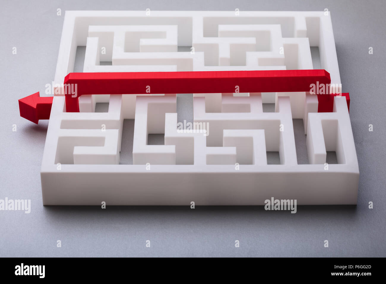 Freccia rossa attraversando il labirinto bianco su sfondo grigio Foto Stock