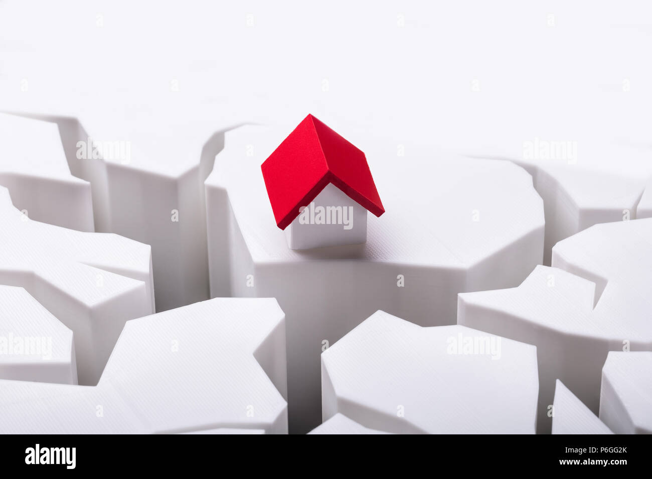 Modello di casa con il tetto rosso isolato su danneggiata la superficie bianca Foto Stock