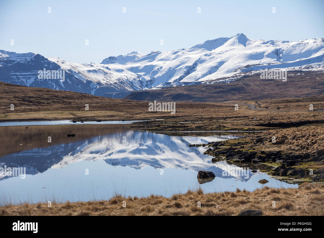 Montagne coperte di neve in Islanda della penisola Snaefellsness sono riflesse nel piccolo lago. Un tratto di strada tranquilla passa attraverso il paesaggio Foto Stock