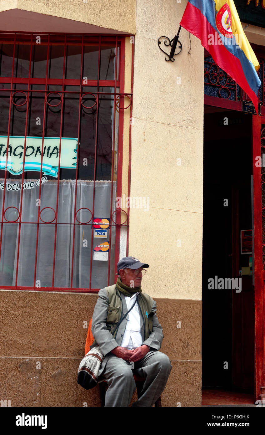 Il vecchio uomo seduto fuori da un bar, prendendo una pausa, bandiera colombiana Foto Stock