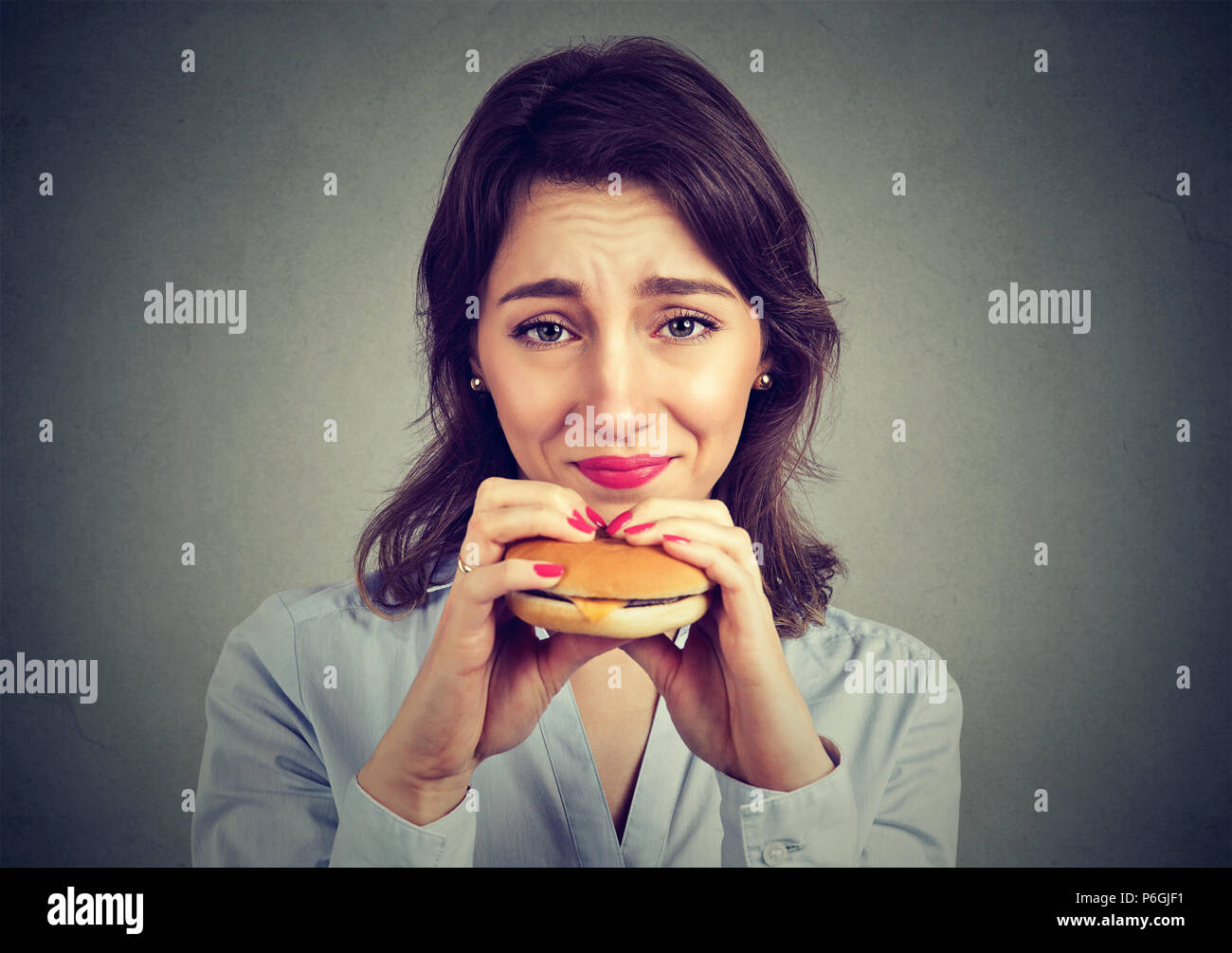 Giovane donna con sentimento di colpa per mangiare un hamburger Foto Stock