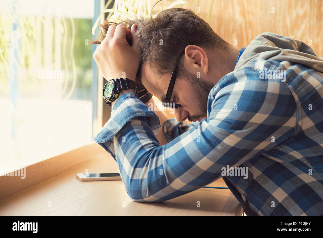 Premuto giovane uomo seduto a tavola con un cellulare in cafe guardando verso il basso essendo infelice con rottura. Foto Stock