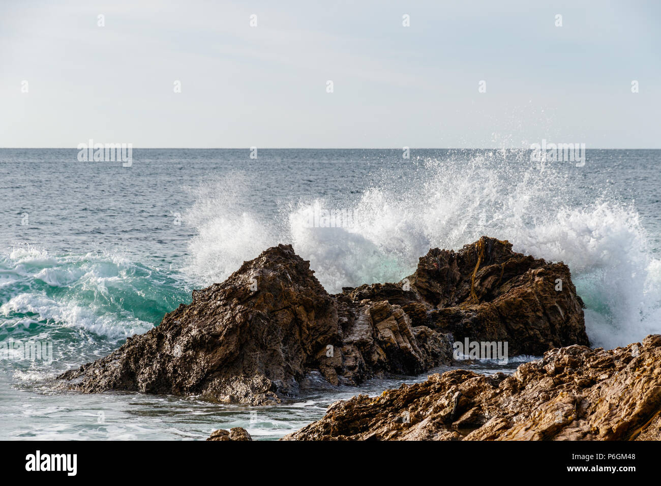 Rottura d'onda su una roccia offshore esposto dalla bassa marea, con l'Oceano Pacifico sullo sfondo; in Crystal Cove parco statale, Laguna Beach in California. Foto Stock