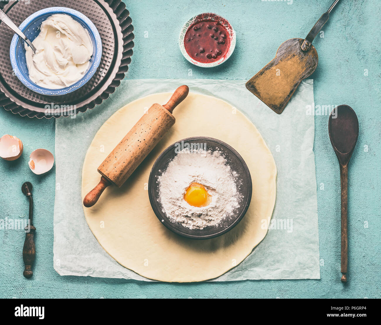 Tasty Baking. Pasta mattarello e ciotola con farina e uova sulla luce blu tavolo da cucina sfondo, vista dall'alto Foto Stock