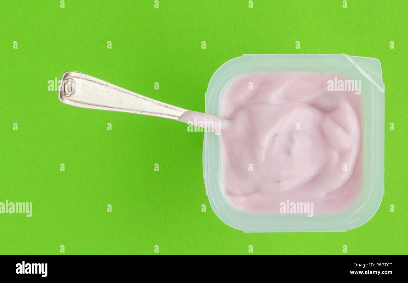 Lo yogurt in una tazza di plastica da vicino con il piccolo cucchiaio d'argento, top view foto di yogurt alla fragola su sfondo verde Foto Stock