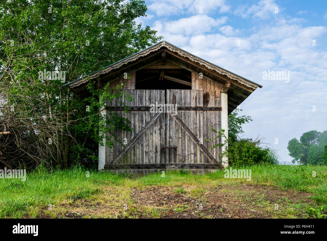 Il vecchio fienile con le nuvole ed erba nella foresta bavarese e un campo di fronte Foto Stock