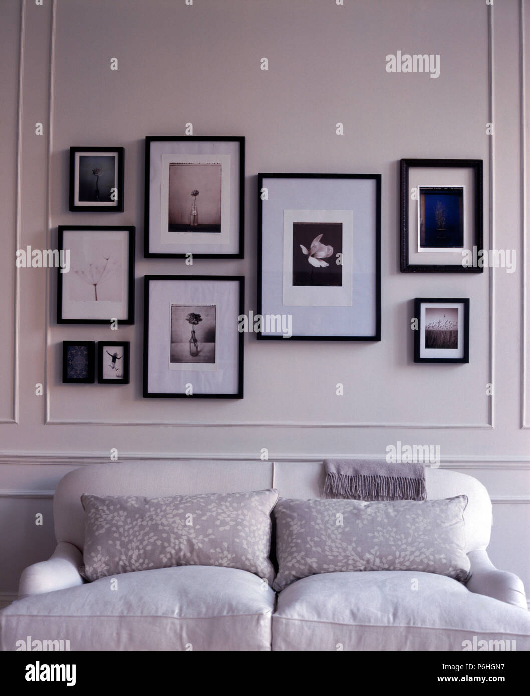 Gruppo di incorniciata nero+fotografie bianco su bianco con pannelli di parete sopra un piccolo divano bianco con cuscini tonificante Foto Stock