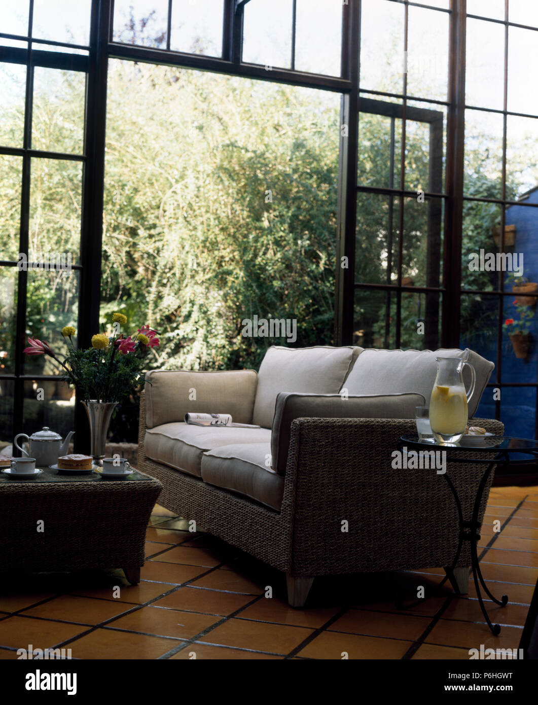 Sisal imbottiti divano e tavolo da caffè in una moderna serra con un pavimento in piastrelle di terracotta e grandi finestre di metallo Foto Stock