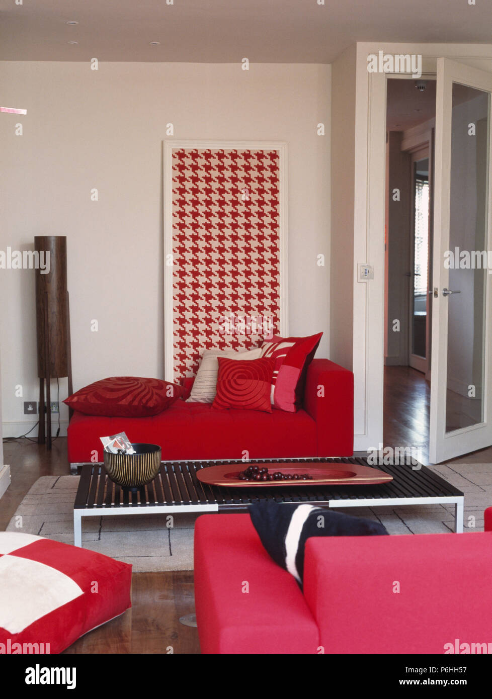 Modellato cuscini rosso su rosso brillante divano nella parte anteriore del grande rosso + bianco hounds-dente immagine in salotto con il caffè nero-tabella Foto Stock