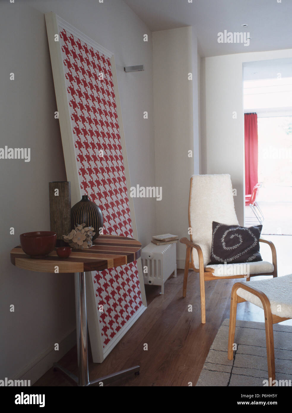 Piccolo piedistallo circolare tabella nel soggiorno moderno con grandi rosso + bianco immagine houndstooth appoggiata contro il muro Foto Stock
