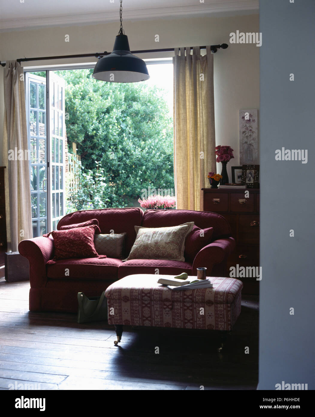 Modellato e ottomano rosa scuro divano in soggiorno con pavimento in legno e fold-back francese windows Foto Stock