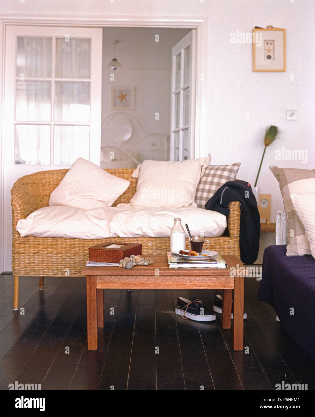 Smple caffè in legno tavolo e divani in vimini con cuscini color crema in piccoli cottage soggiorno con dipinta di nero floorbboards Foto Stock