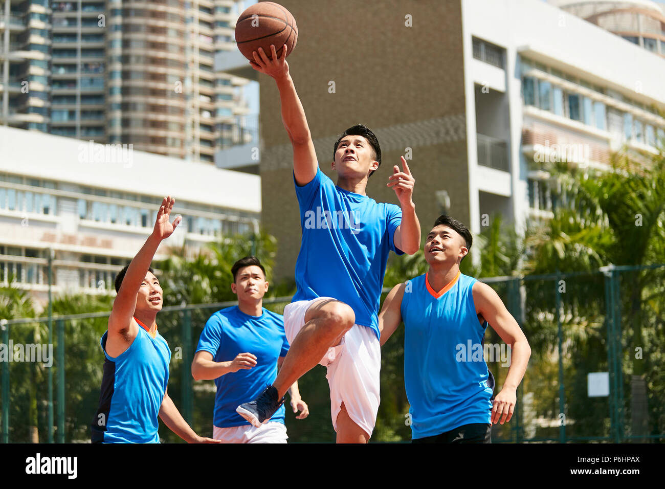 Giovani asiatici maschio adulto giocatore giocare la pallacanestro su un urbano corte esterna. Foto Stock