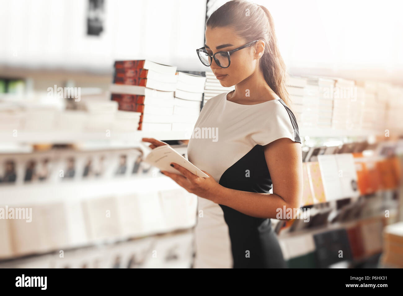 Giovane donna attraente la lettura di libro in un book store accanto a scaffale. Foto Stock